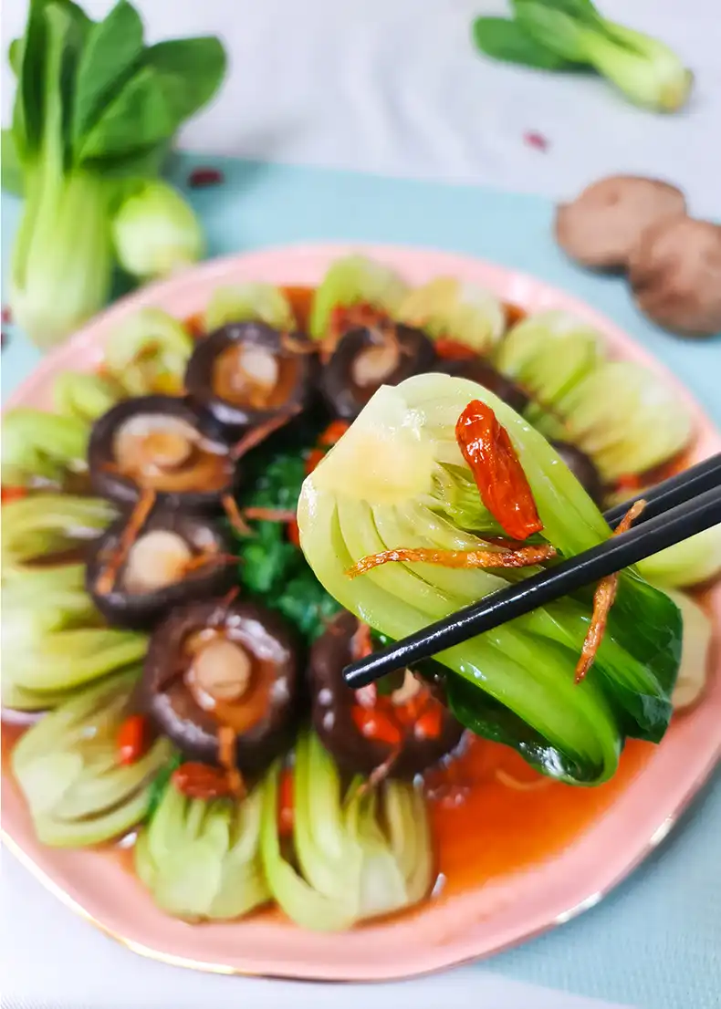 lets eat A pair of chopsticks holding up bok choy, topped with ginger.