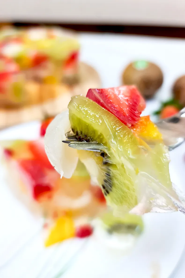 lets eat Kiwi, strawberries and longan in a jelly cake piece on a fork.