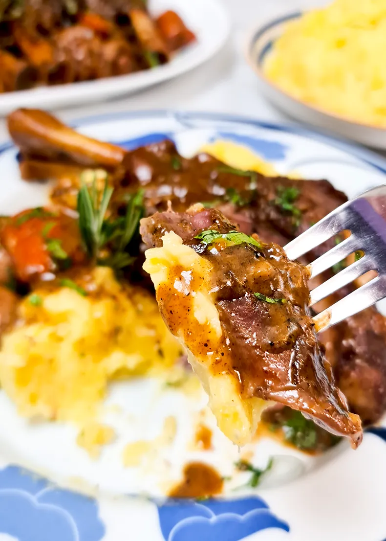 lets eat A fork holding up a piece of lamb meat and some mashed potato with gravy.